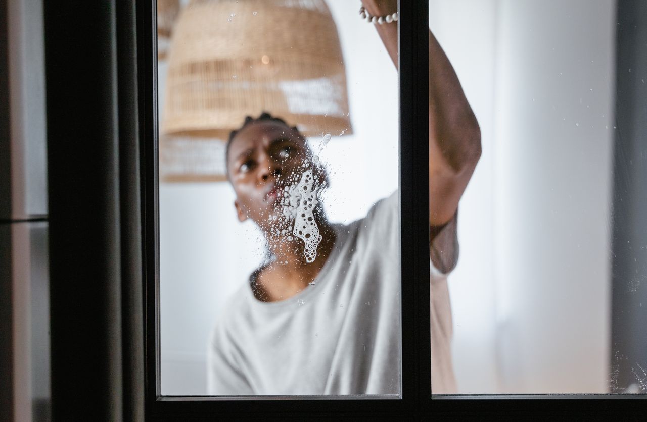 Un homme adulte nettoie une vitre en intérieur, en se concentrant sur les tâches ménagères et la propreté.